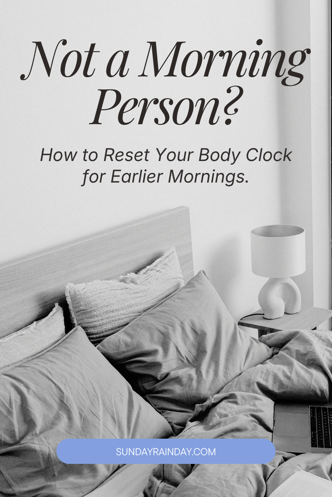 Pin titled “Not a Morning Person? How to Reset Your Body Clock for Earlier Mornings”, over a calm black-and-white bedroom with an unmade bed in soft linen, layered pillows, a sculptural lamp and a laptop.