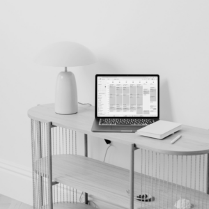Black-and-white photo of a minimalist console table with a white mushroom lamp, a closed notebook and a laptop showing a weekly calendar filled with time blocks, for an article about using time blocking to protect time for your whole life.
