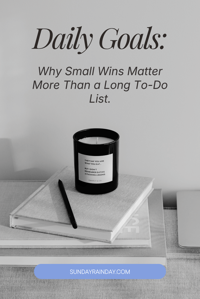 Minimalist black-and-white desk scene with a candle on a linen notebook and a pencil, under the title “Daily Goals: Why Small Wins Matter More Than a Long To-Do List”.