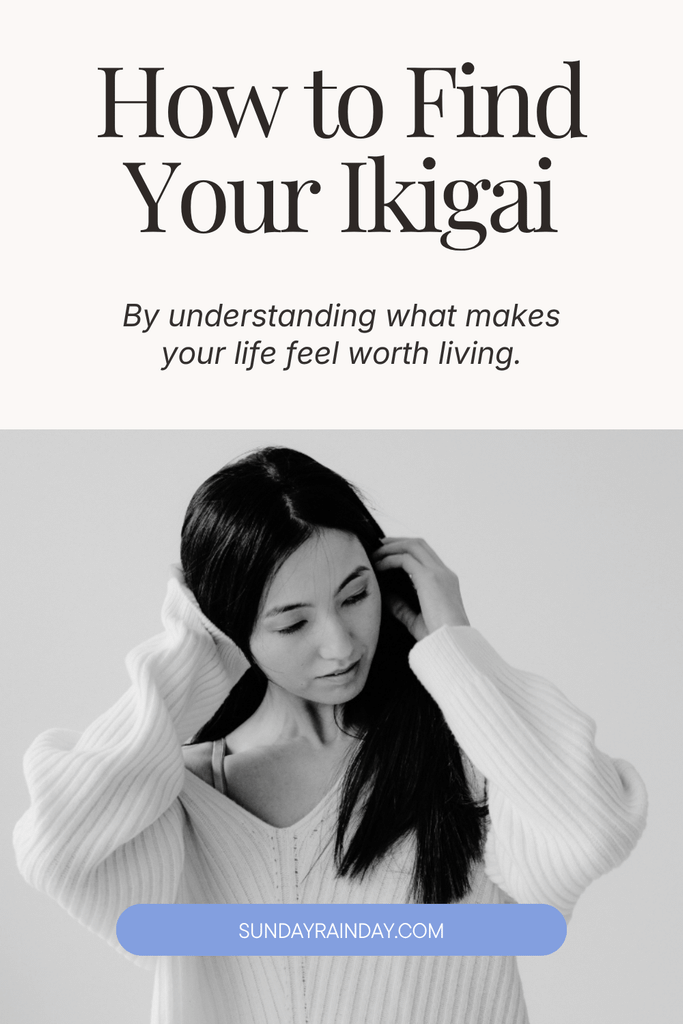 How to find your ikigai by understanding what makes your life feel worth living, shown above a black-and-white photo of a woman with long dark hair in a white knit jumper, looking down with her hands in her hair