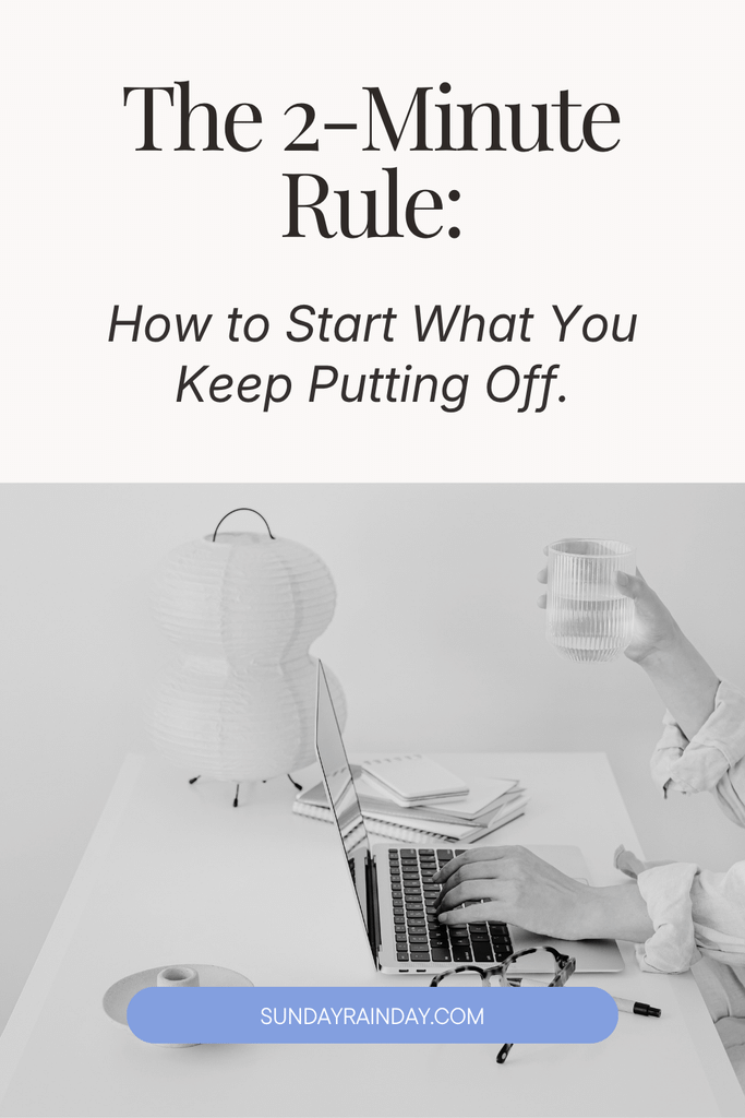 The 2-minute rule: how to start what you keep putting off, shown above a black-and-white photo of a person typing on a laptop at a desk while holding a glass of water