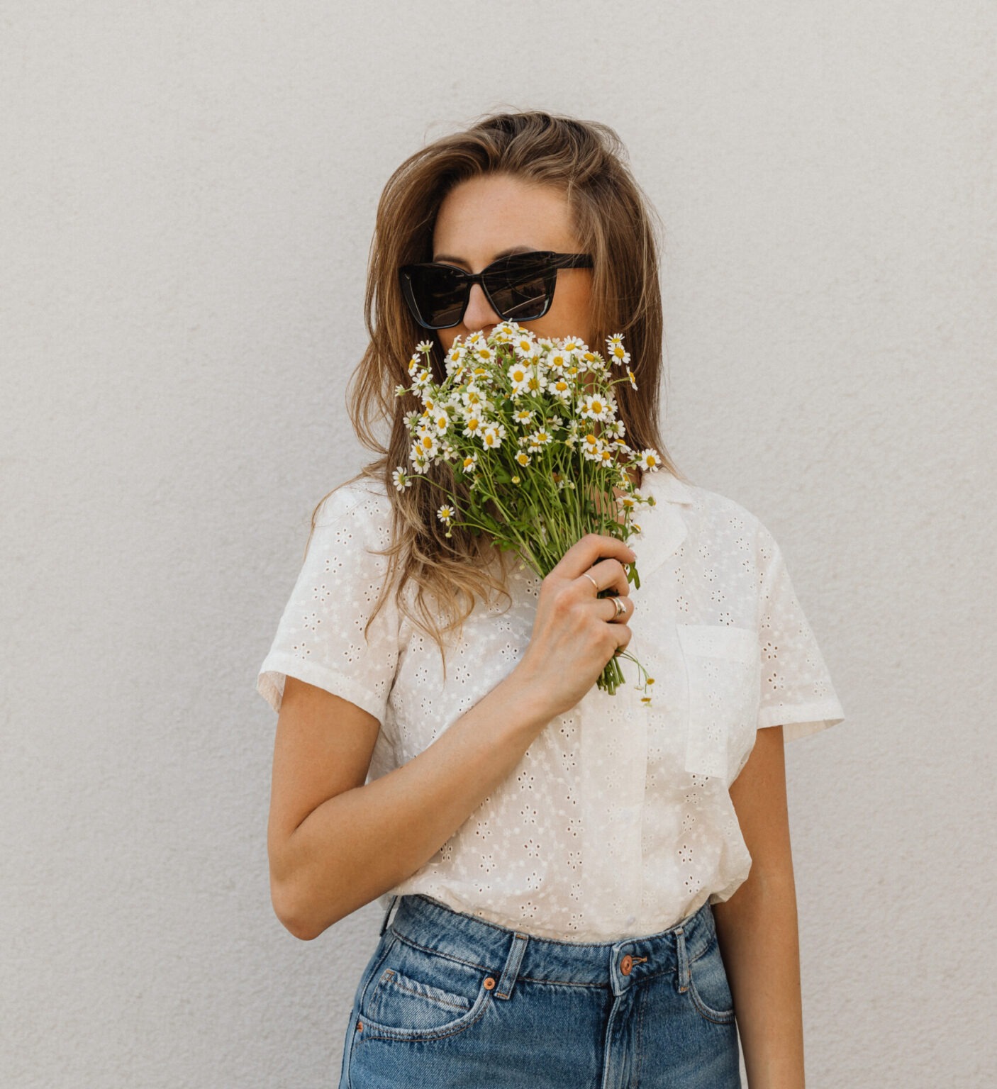 woman in white shirt, blue jeans holding a bouquet of flowers