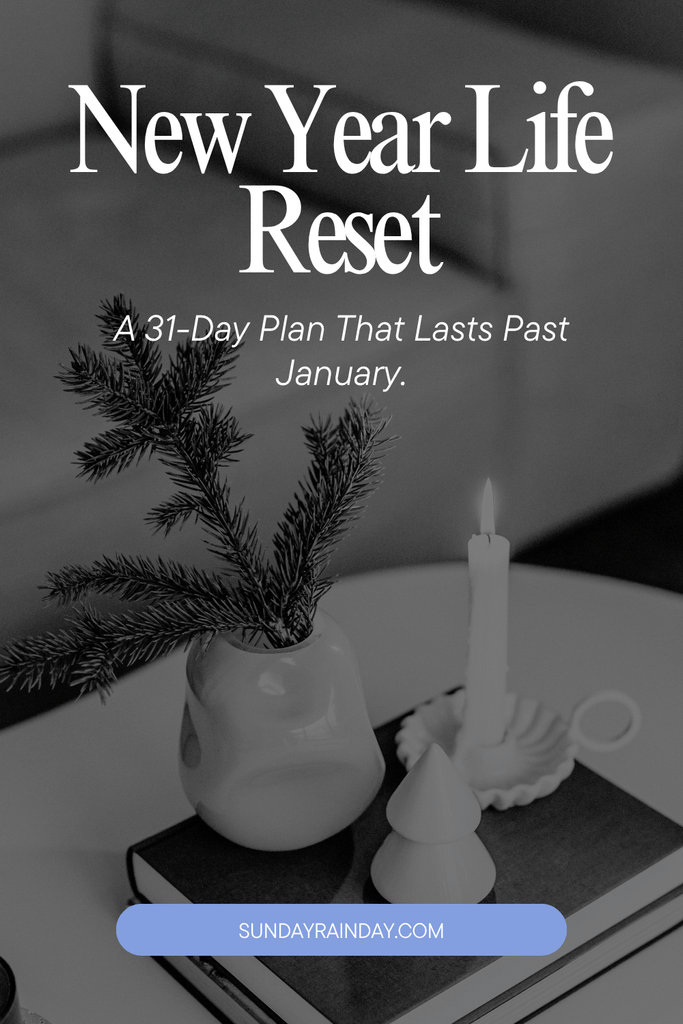 Black-and-white pin reading “New Year Life Reset: A 31-Day Plan That Lasts Past January”, over a candle, a small ceramic tree and a vase of fir branches on a book.