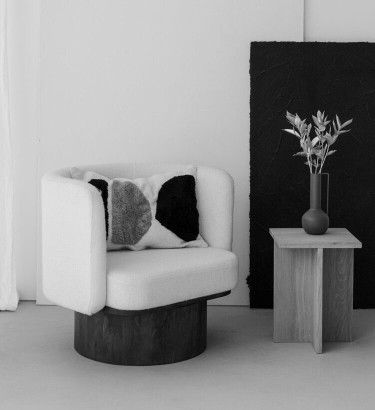 Black and white photo of a calm, minimalist room with a bouclé armchair, a wooden side table and dried flowers