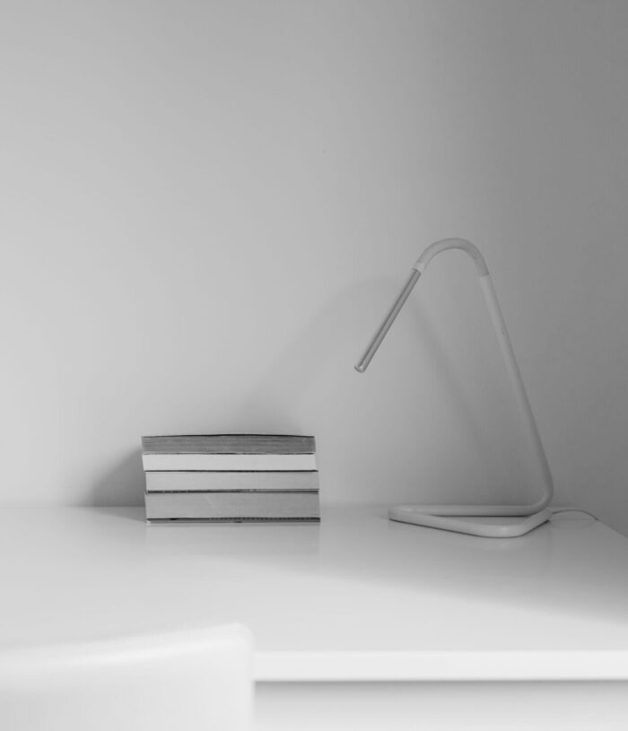 Black and white photo of a clear white desk with a small stack of books and a slim desk lamp, for the Focused Productivity section