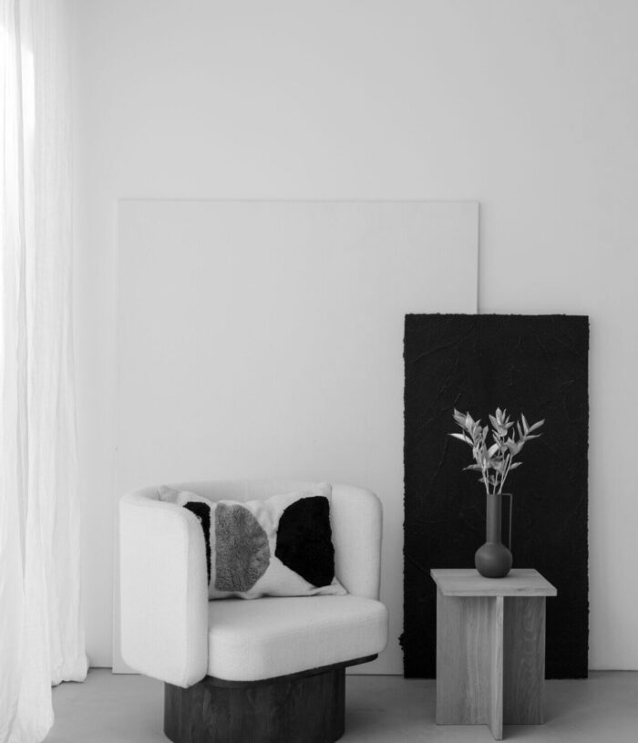 Black and white photo of a minimalist corner with a bouclé armchair, a wooden side table and a vase of dried flowers, for the Habits and Routines section