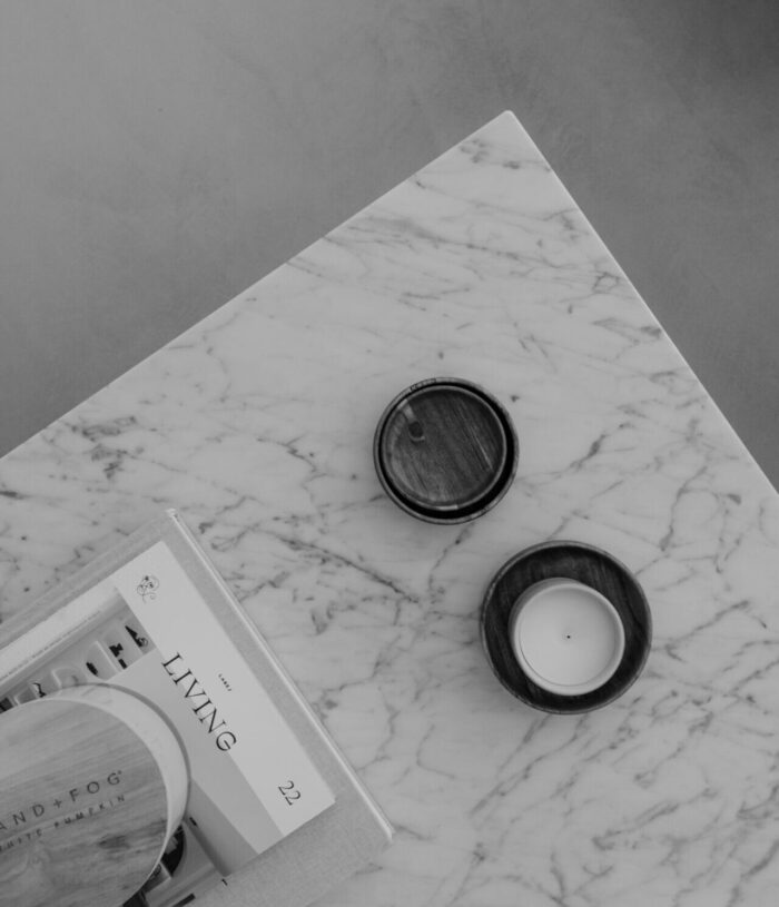Black and white photo of a marble table seen from above, with two candles in wooden holders and a stack of magazines, for the Self-Discovery section